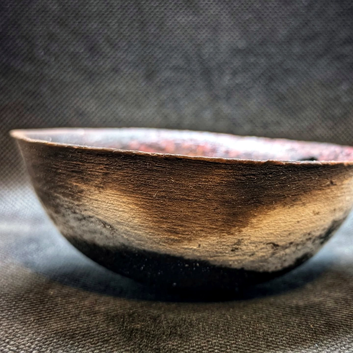 Low bowl viewed from above, with a pink-red crackle interior, darkened centre and small owl motif near the rim.