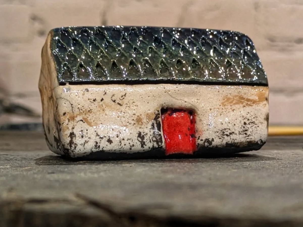 Finished raku croft house with a dark glazed roof, pale walls and a red door.